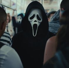 a group of people in black and white costumes with ghost masks on their faces, all looking at the camera