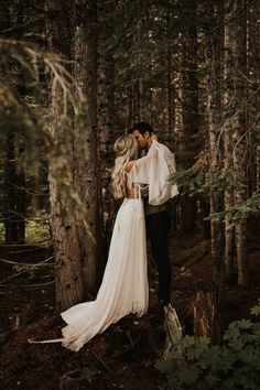 a bride and groom standing in the woods hugging each other with their arms around each other