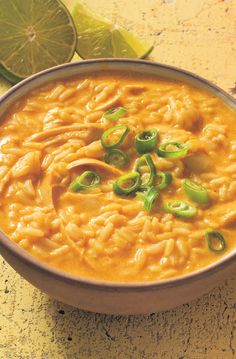 a bowl filled with macaroni and cheese on top of a table next to limes