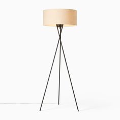 the tripod floor lamp has a beige shade on it