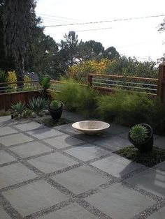 a stone patio with two black planters and a white bowl on the ground next to it