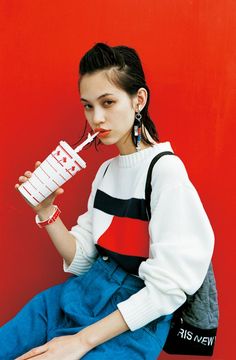 a woman sitting on the ground with a drink in her hand and wearing a sweater