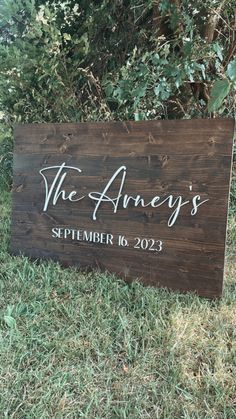 a wooden sign sitting in the grass next to some bushes and trees, that says the ancy's