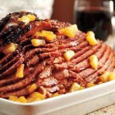 a white bowl filled with meat and pineapple toppings next to a glass of wine