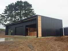 a large black building sitting on top of a dirt field next to trees and grass