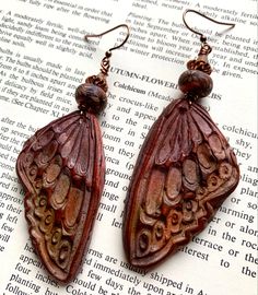 a pair of brown earrings sitting on top of an open book with beads hanging from it