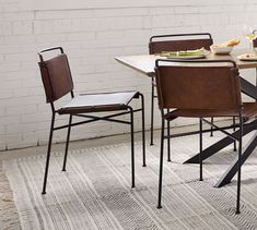 a dining room table with chairs and plates on it, next to a brick wall