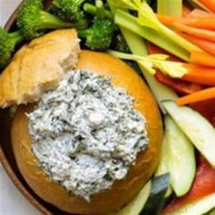 a bowl filled with vegetables and dip on top of a bagel roll next to broccoli