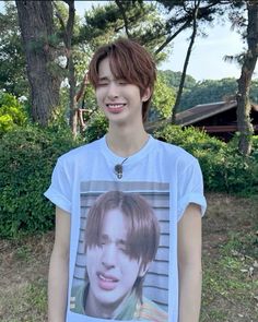 a young man standing in front of trees and bushes wearing a t - shirt with an image of him on it