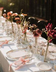 a long table is set with plates and vases filled with flowers on top of it