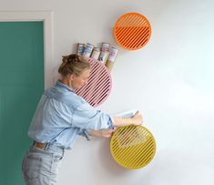 a woman leaning against a wall holding a yellow and orange rack with magazines on it