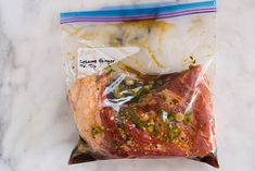 a piece of meat wrapped in plastic sitting on top of a marble counter next to a bag of seasoning