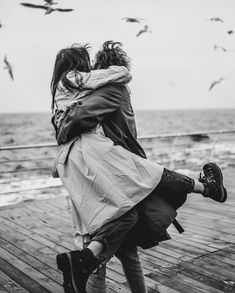 black and white photograph of two people embracing each other on a pier with seagulls in the background