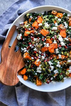 a white bowl filled with lots of food on top of a blue cloth next to a wooden spoon