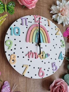 a clock with numbers and a rainbow painted on the face, surrounded by pink flowers