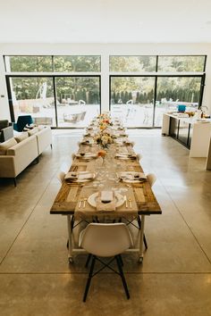 a long table set up with plates and place settings in front of large glass windows