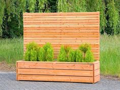 a wooden planter box with plants in it on a brick walkway next to grass and trees