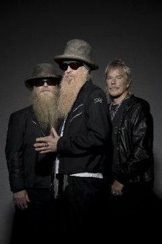 two men with long beards standing next to each other in front of a dark background