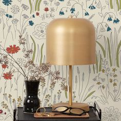 a table with a lamp and glasses on it next to a wallpapered background