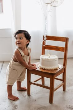 a small child standing next to a wooden chair with a cake on top of it