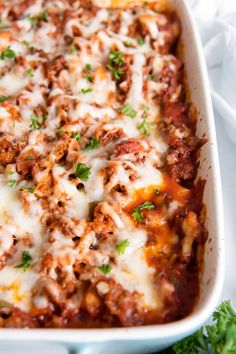 a casserole dish with meat, cheese and parsley in it on a white cloth