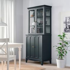 a black china cabinet with glass doors in a white dining room setting next to a potted plant