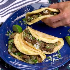 a blue plate topped with three tacos covered in meat