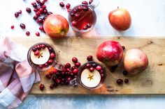 apples and cranberries on a cutting board next to some glasses with liquid in them