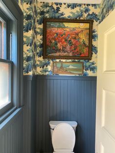 a white toilet sitting in a bathroom next to a painting on the wall above it