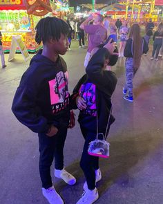 two young men standing next to each other in front of carnival rides at night time