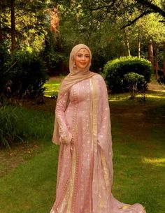 a woman in a pink and gold dress standing on grass with her hands behind her head