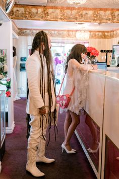 two people standing in front of a counter with flowers on it and one person holding a pink purse