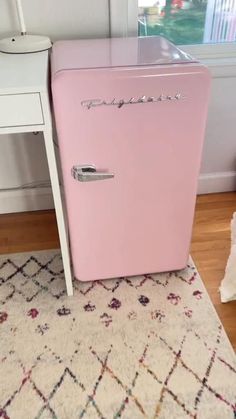 a pink refrigerator sitting on top of a rug next to a white table and chair