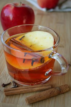 an apple cider and cinnamon sticks sit on a wooden table next to two apples