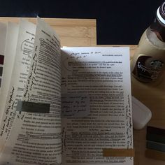 an open book sitting on top of a wooden table next to a cup of coffee