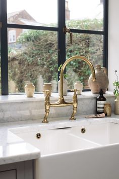 a kitchen sink with gold faucet and white counter top next to a window