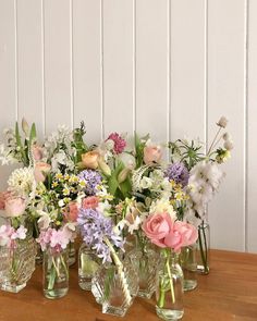 a group of vases filled with flowers sitting on top of a wooden table in front of a white wall