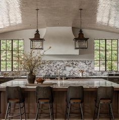 a large kitchen with marble counter tops and stools in front of an island that has four lights hanging from the ceiling