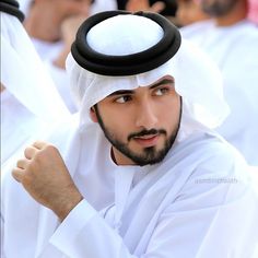 a man wearing a white and black headdress is posing for the camera with other people in the background