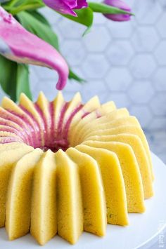 a yellow cake with pink flowers in the background on a white platter, ready to be eaten