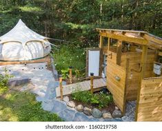 a yurt in the woods with an outhouse and garden area, near trees