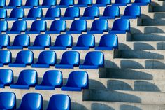 rows of blue chairs sitting next to each other in front of cement steps with shadows on them