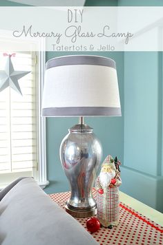 a lamp on a table next to a bed with blue walls and white curtains in the background