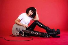 a woman sitting on the ground with a guitar in front of her, wearing black leather pants and boots