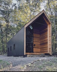 a small cabin in the woods with its door open and wood sidings on it