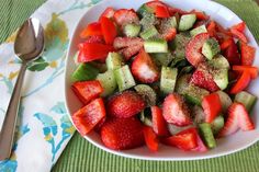 a white bowl filled with sliced up strawberries and cucumbers next to a fork