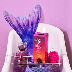 there is a purple mermaid tail on the shelf next to a wine glass and box