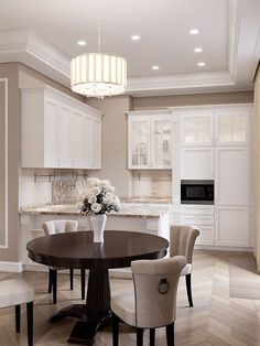 an instagram photo of a dining room and kitchen with white cabinets, chandelier, marble countertops, and round table