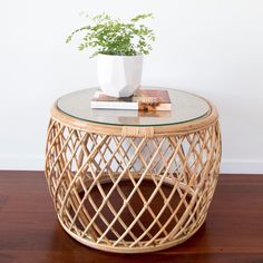 a wicker table with a glass top and books on the bottom, next to a potted plant