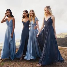 three beautiful women in long dresses standing on the side of a hill looking at the camera